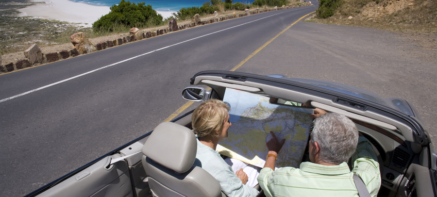 Photo of a senior couple driving in a comfortable by the ocean,  looking at a map.